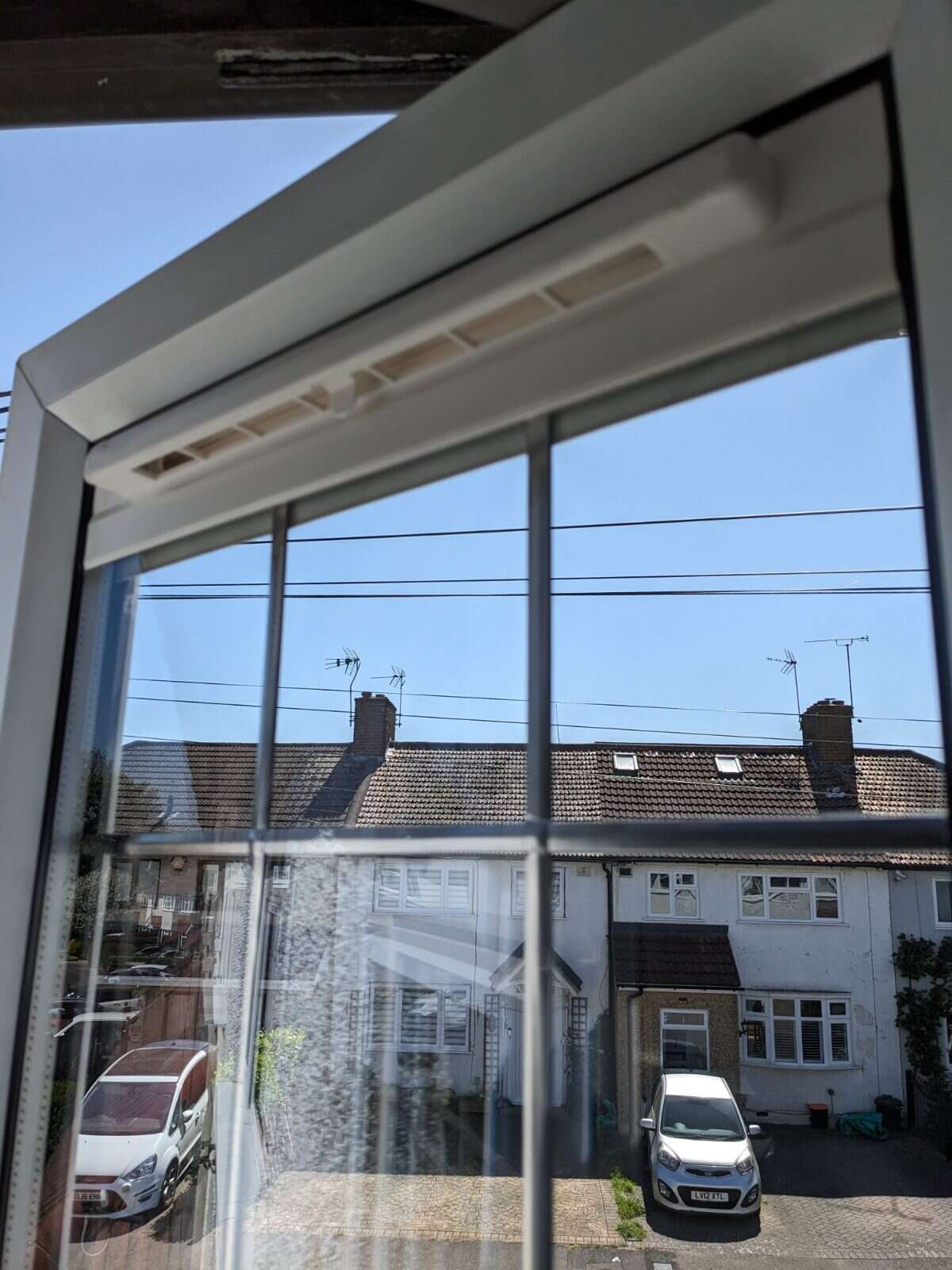 Slimline Glass Vent fitted along the top rail of a bedroom window looking over rooftops